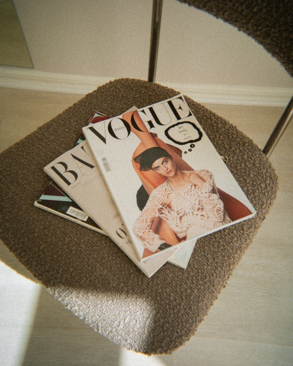A stack of fashion magazines on a boucle chair in afternoon light
