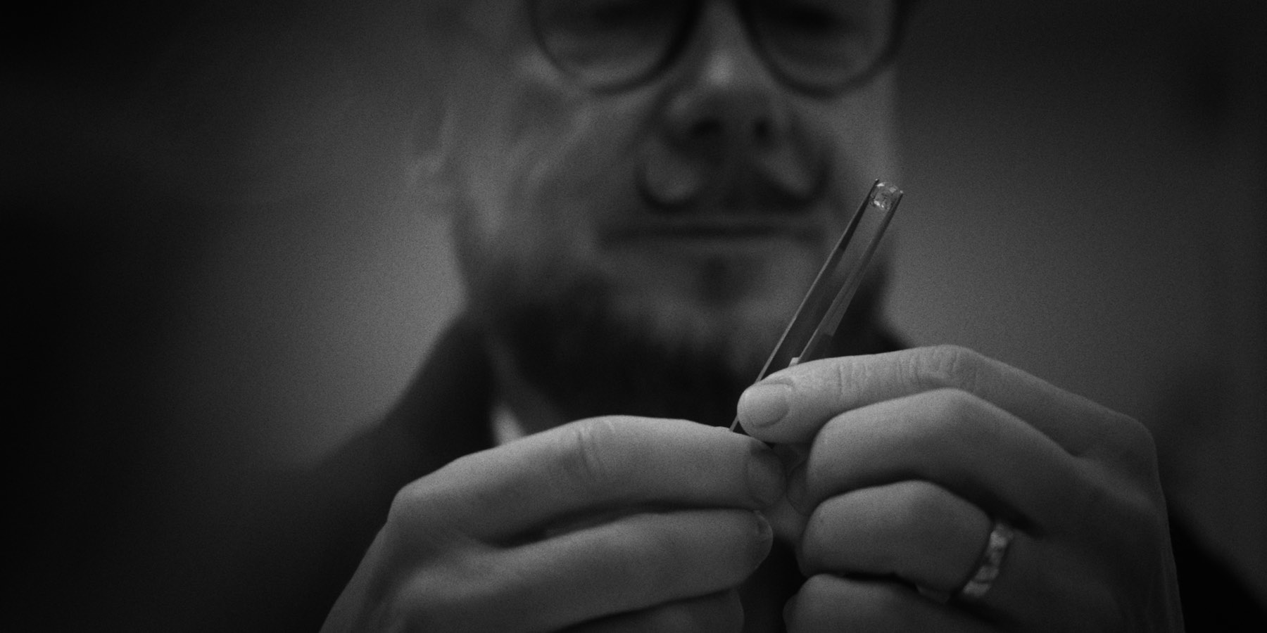 A goldsmith examining a stone with tweezers, in black and white, from a managed brand's content shoot