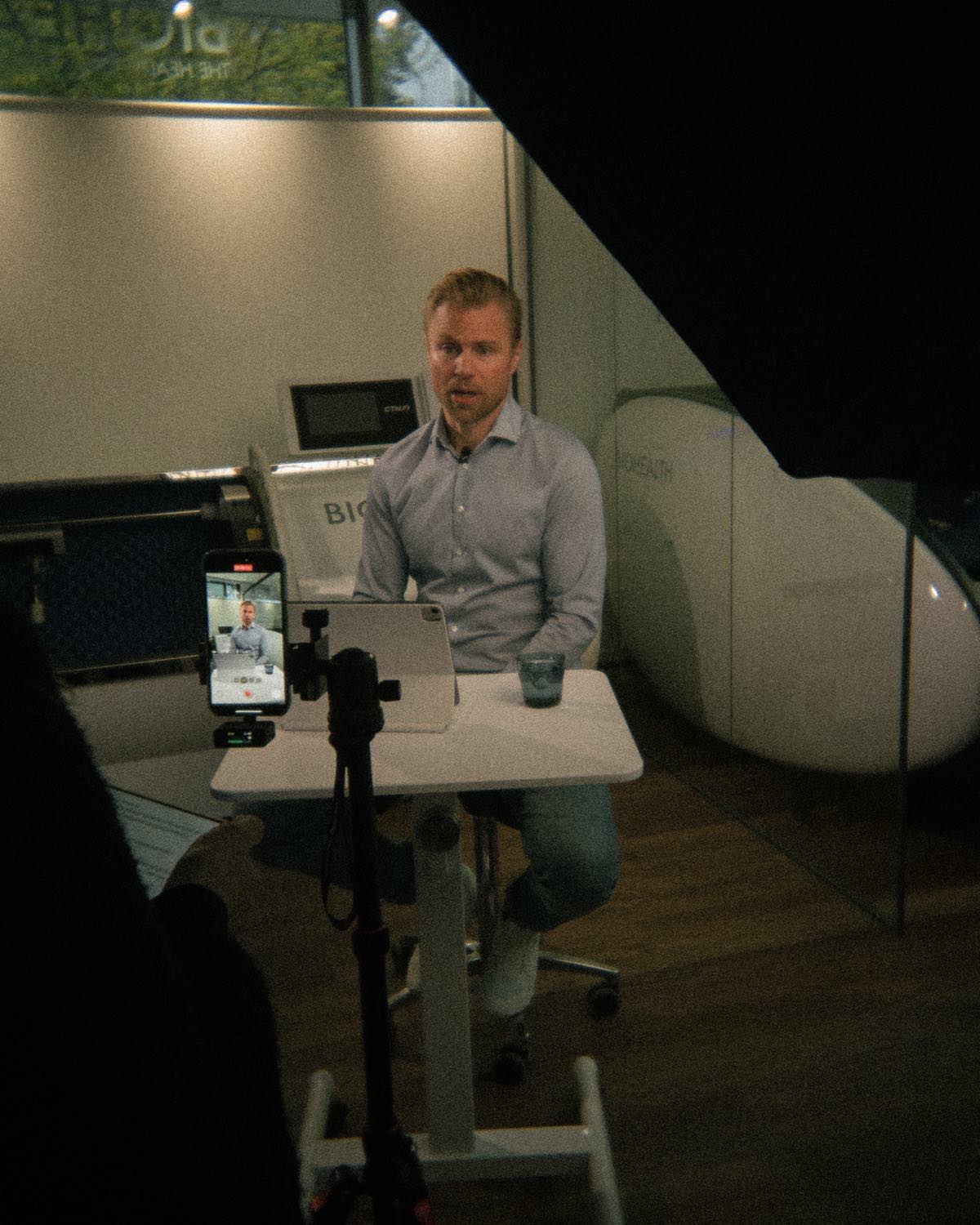 A founder filmed at his desk for Biohealth, phone rig and teleprompter in frame