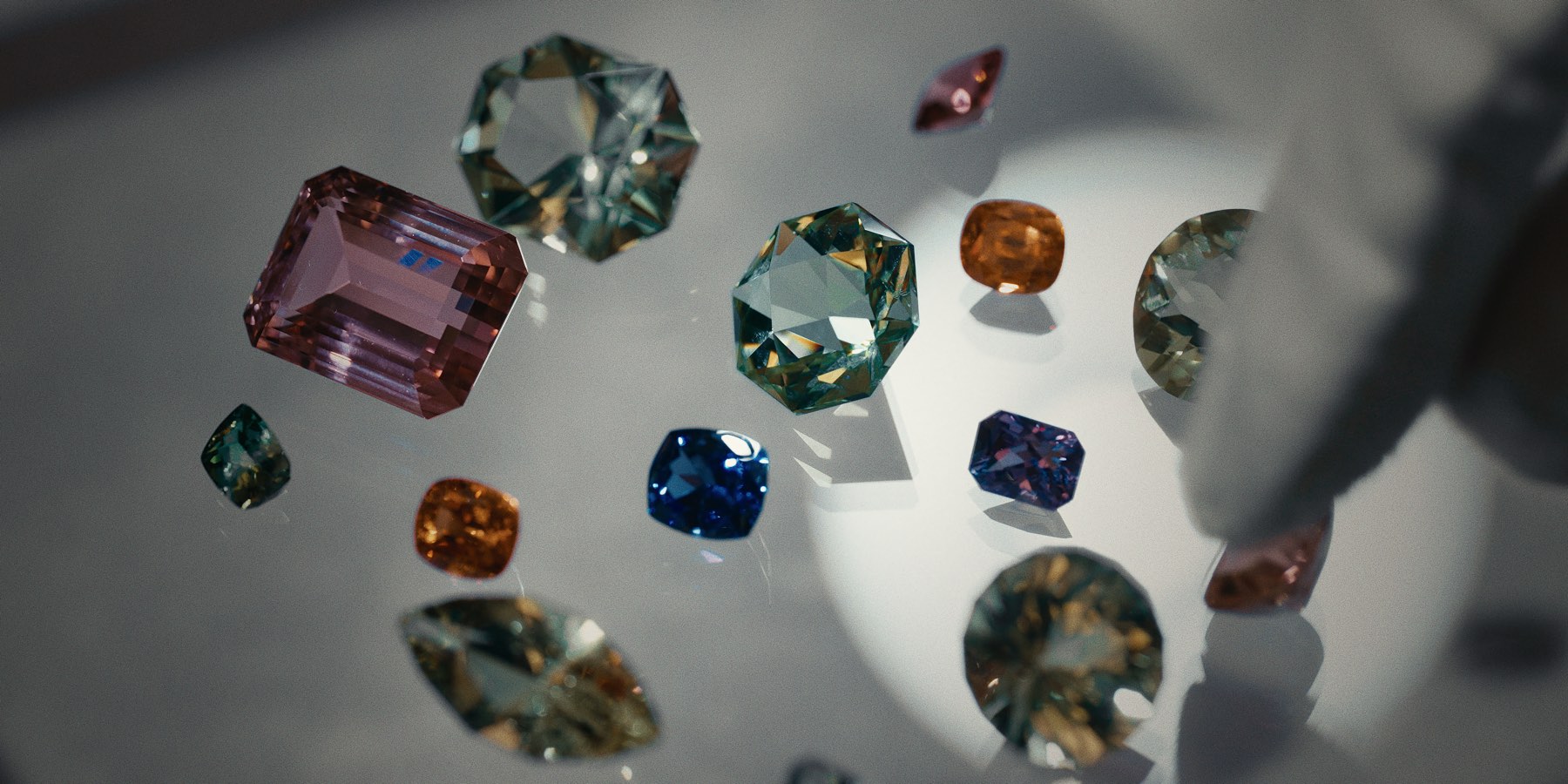 Loose coloured gemstones laid out on a table, a hand reaching in from the side