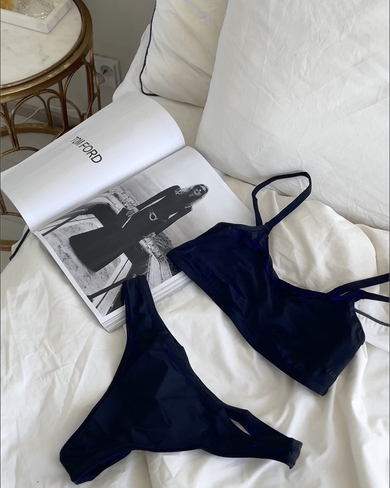 A flat lay on white bedding: swimwear beside an open magazine