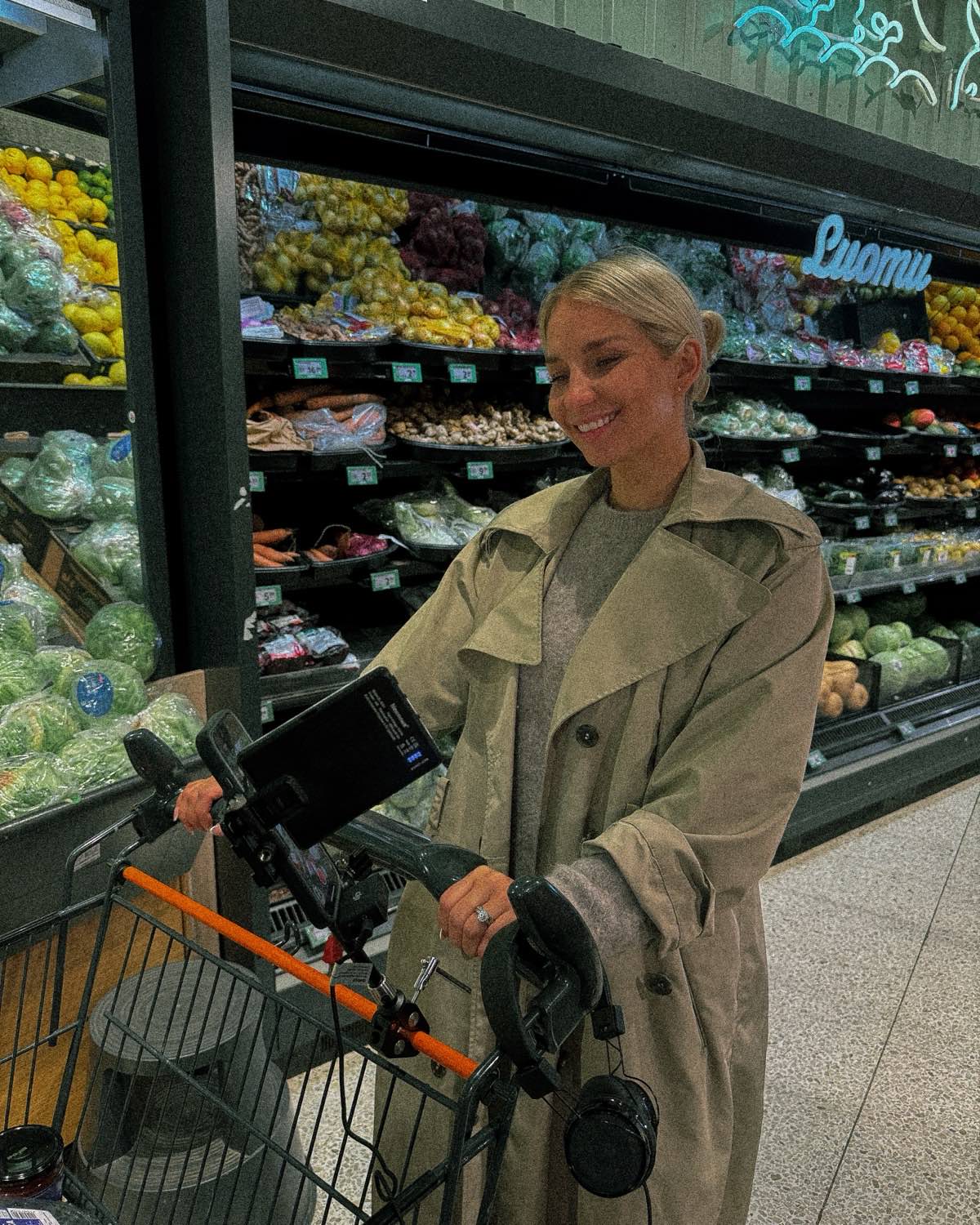 Talent smiling to camera beside the produce shelves, the rig on the trolley