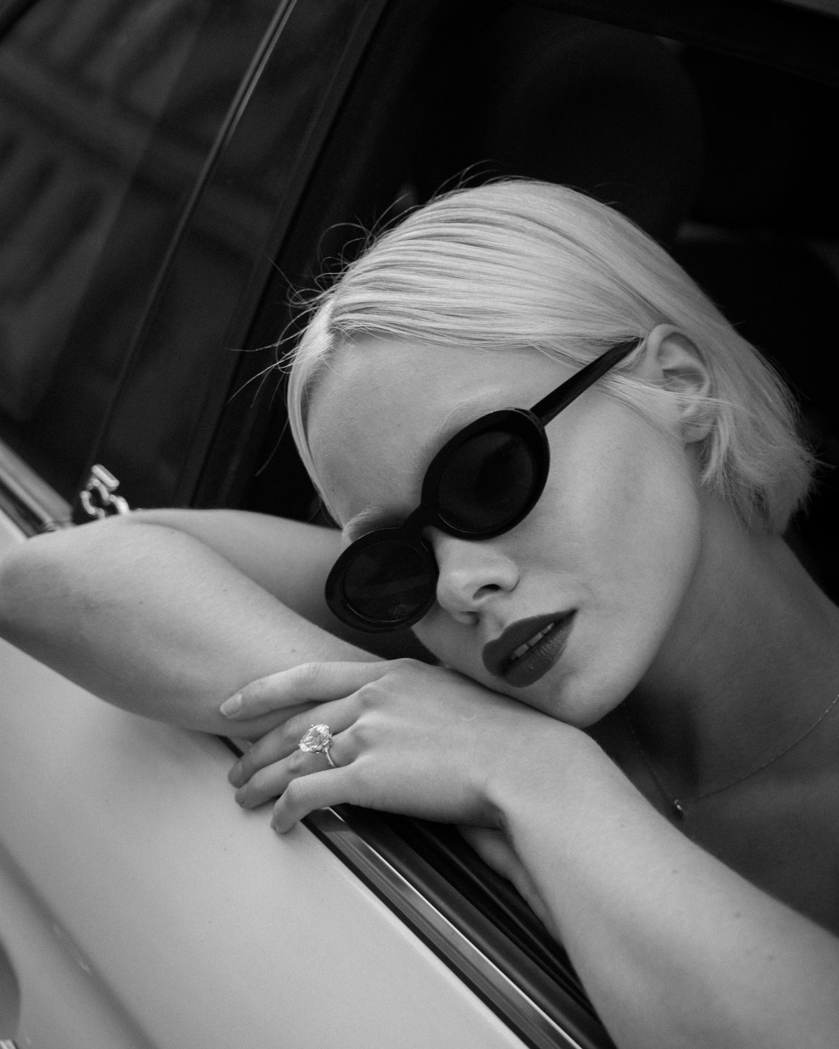 A creator in sunglasses leaning out of a car window, black and white