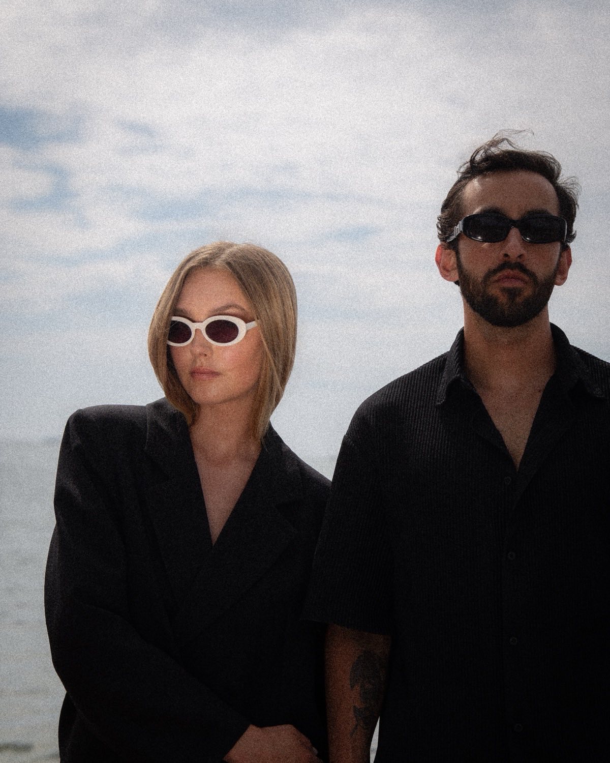 A couple in black sunglasses photographed against the sea