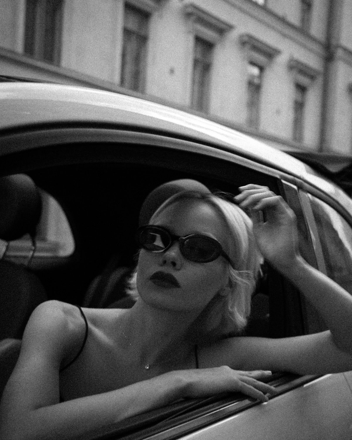 A woman in sunglasses leaning out of a car window, black and white